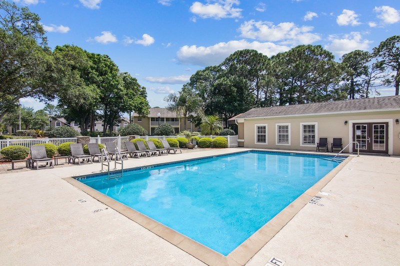 A large swimming pool surrounded by trees and chairs.