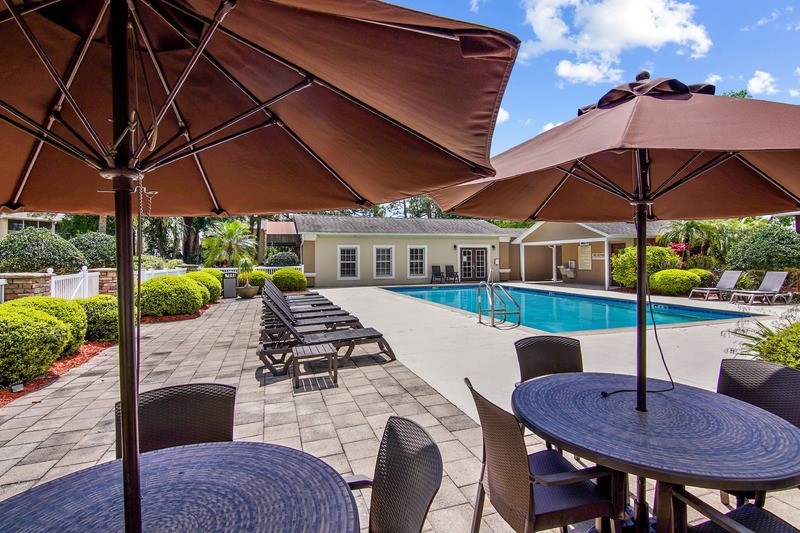 A patio with a table, chairs and umbrellas overlooking a pool.