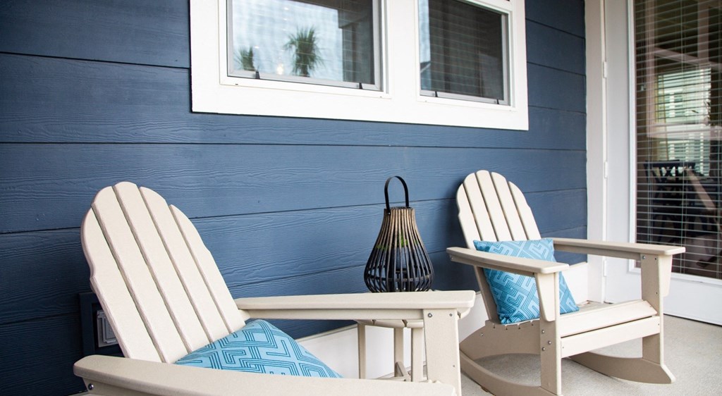 two white rocking chairs with blue pillows sitting on a porch with a blue wall