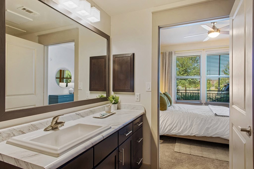 a bathroom with a sink and a mirror and a bedroom with a bed