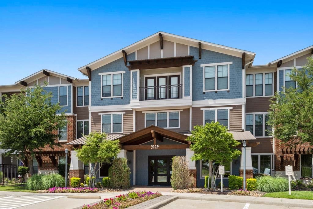 an apartment building with a driveway and trees in front of it