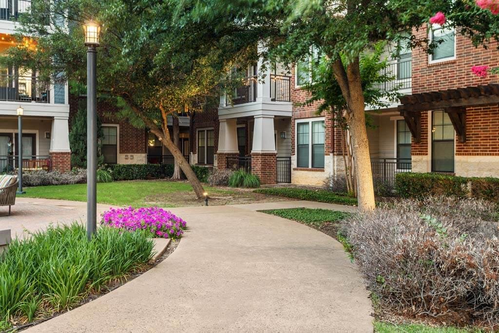 a sidewalk in front of a building with trees and flowers