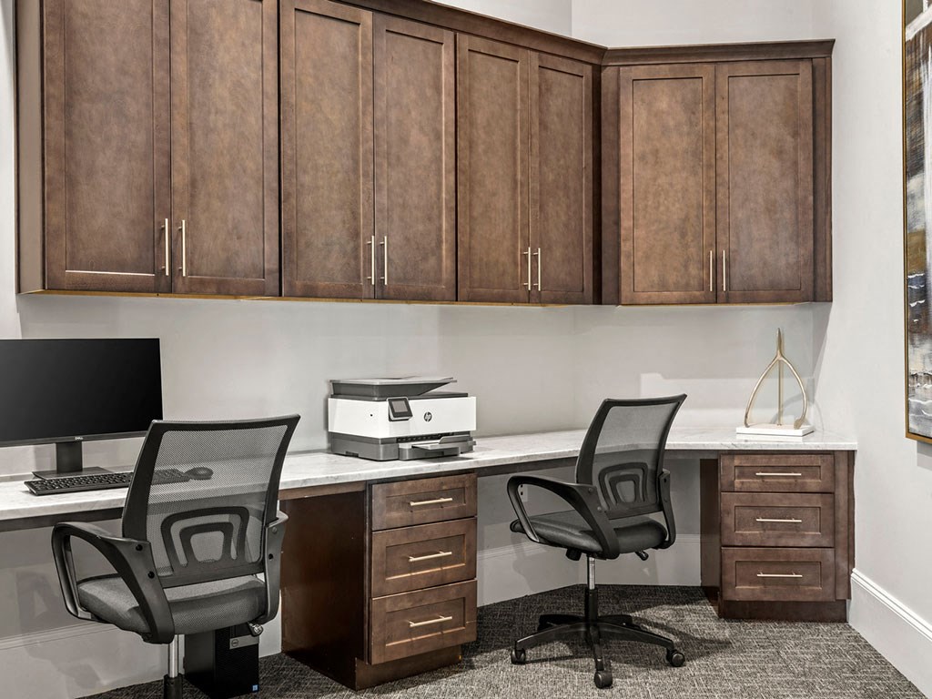 Two black chairs are in front of a desk with a monitor, keyboard, and a printer.