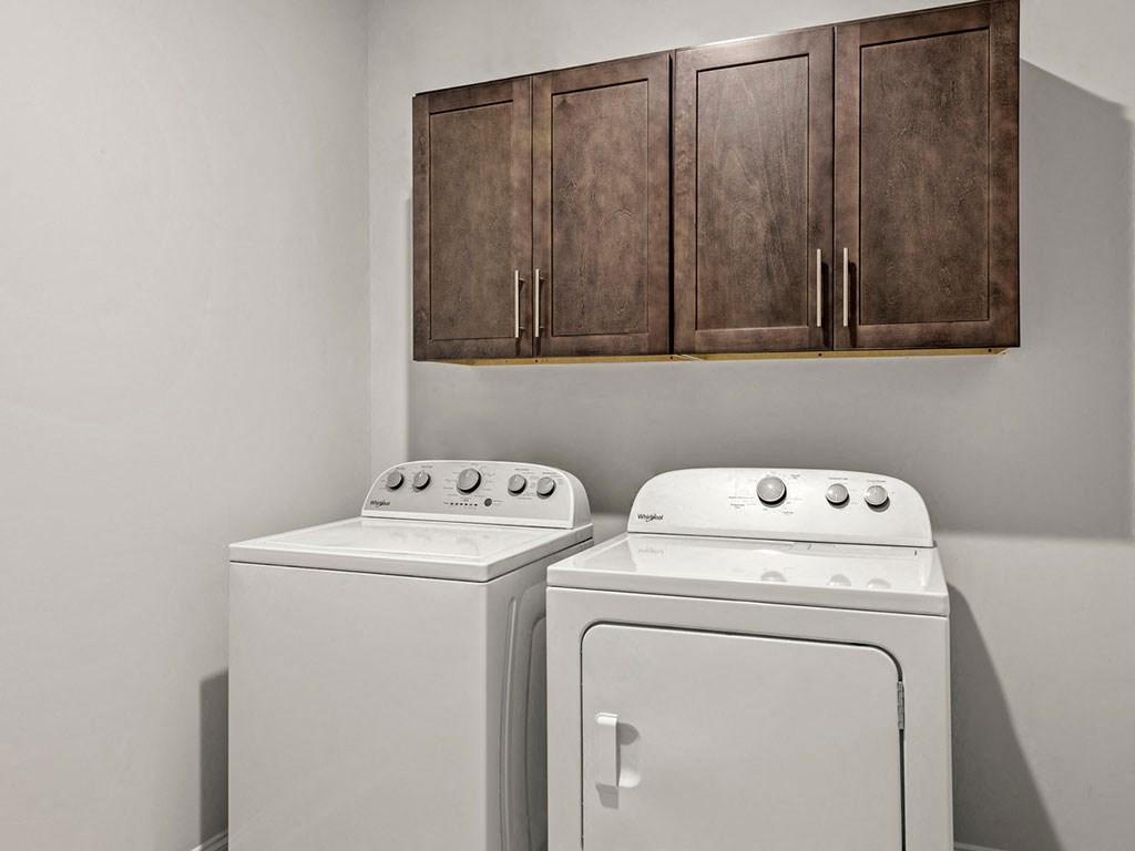 Two white washing machines in front of brown cabinets.