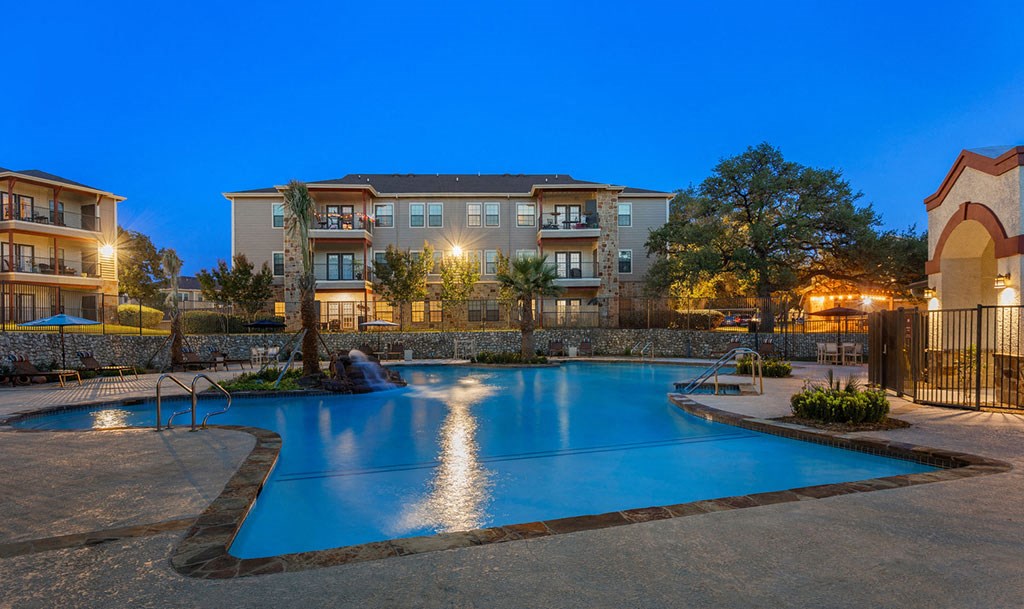 a swimming pool at night with an apartment building in the background
