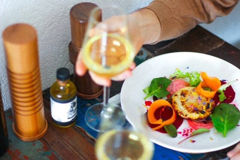 a person holding a glass of wine over a plate of food