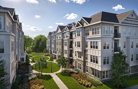 A row of white apartment buildings with green lawns and trees in front.