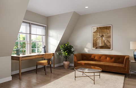 A living room with a brown couch, a desk with a chair, a potted plant, and a framed picture on the wall.