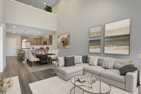 A modern living room with a grey sofa, a glass coffee table, and a dining table set up.