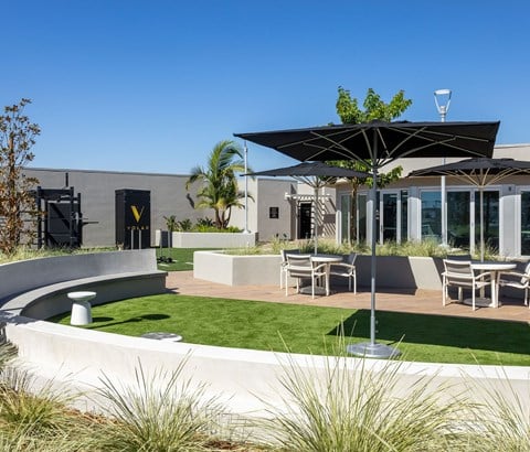 A modern outdoor seating area with a curved bench and a table under a black umbrella.