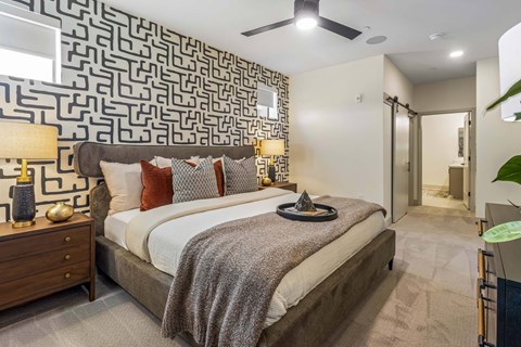 A bedroom with a patterned wallpaper and a bed with a grey blanket.