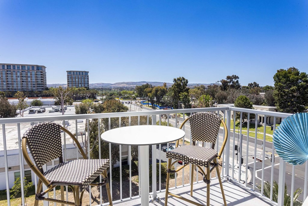 A balcony with a table and chairs overlooking a cityscape.