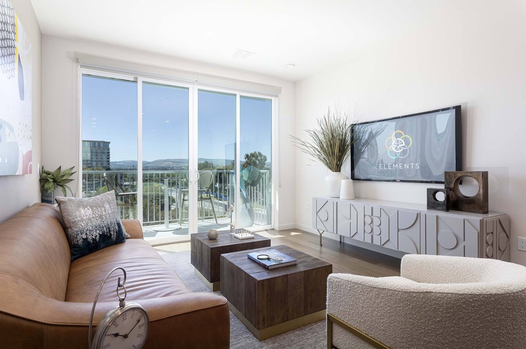 A living room with a brown leather couch, a white chair, and a flat screen TV mounted on the wall.