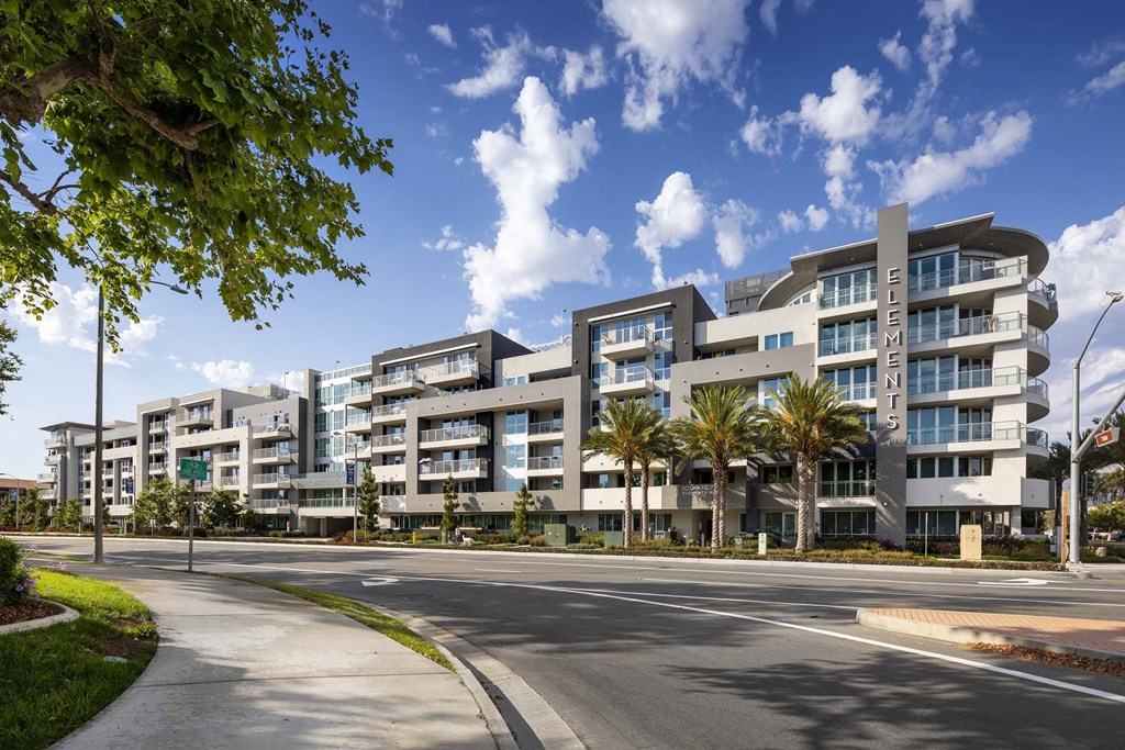 A modern apartment complex with a curved design is surrounded by trees and a clear sky.