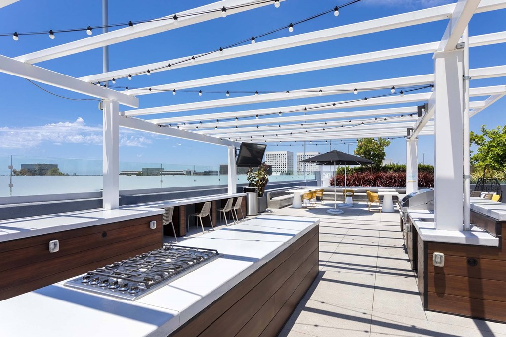 A rooftop patio with white tables and chairs under a white pergola.