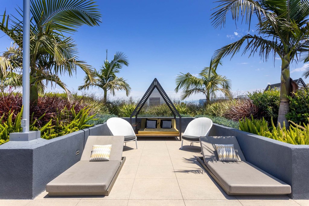 A patio with two lounge chairs and a table with a white cushion and a yellow tablecloth.