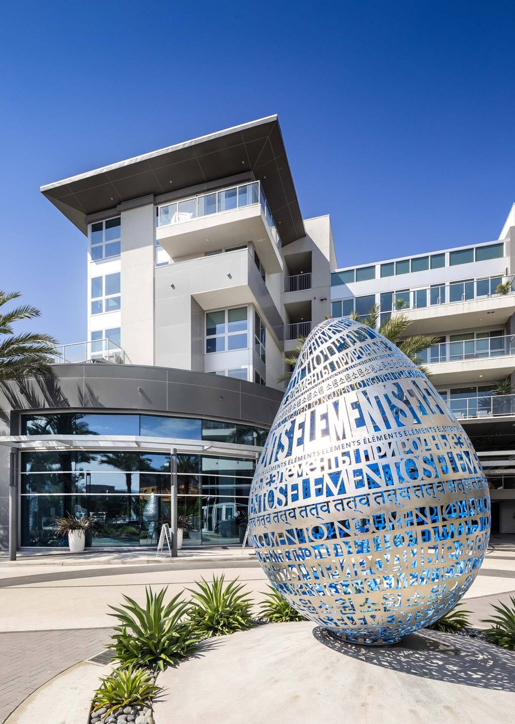 A large blue egg-shaped sculpture with words written on it in front of a modern building.