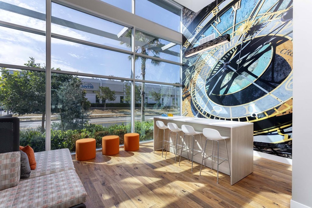 A large clock is on the wall in a room with a bar and stools.