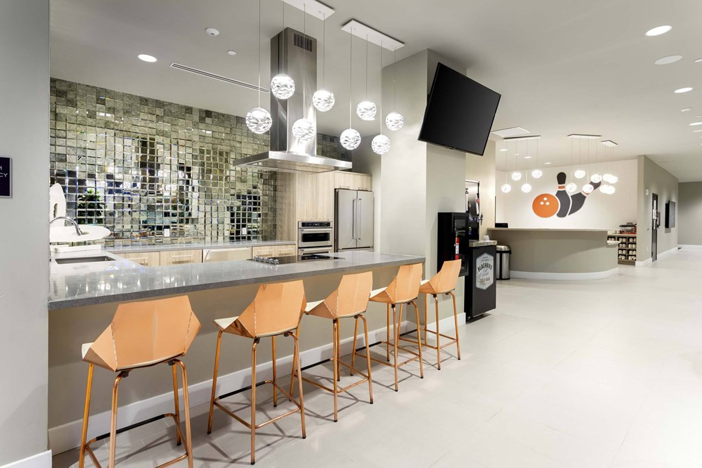 A modern bar with orange chairs and a black screen on the wall.