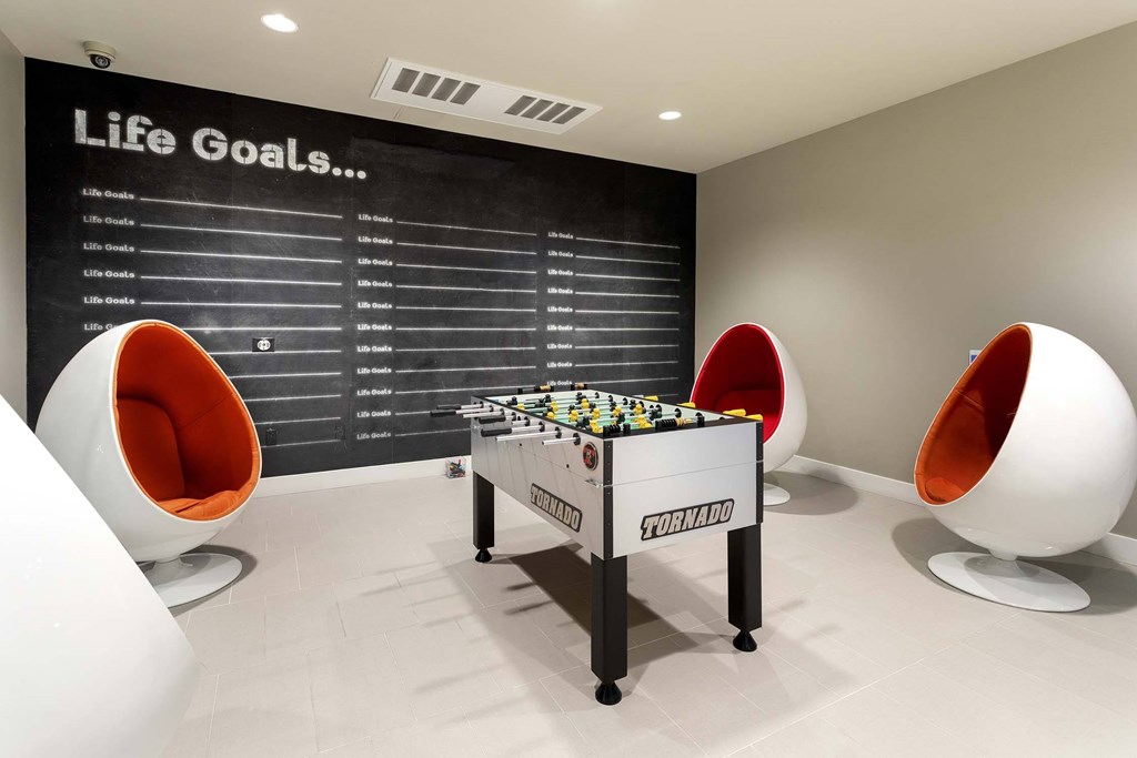 A game of table football is set up in a room with a blackboard listing life goals.