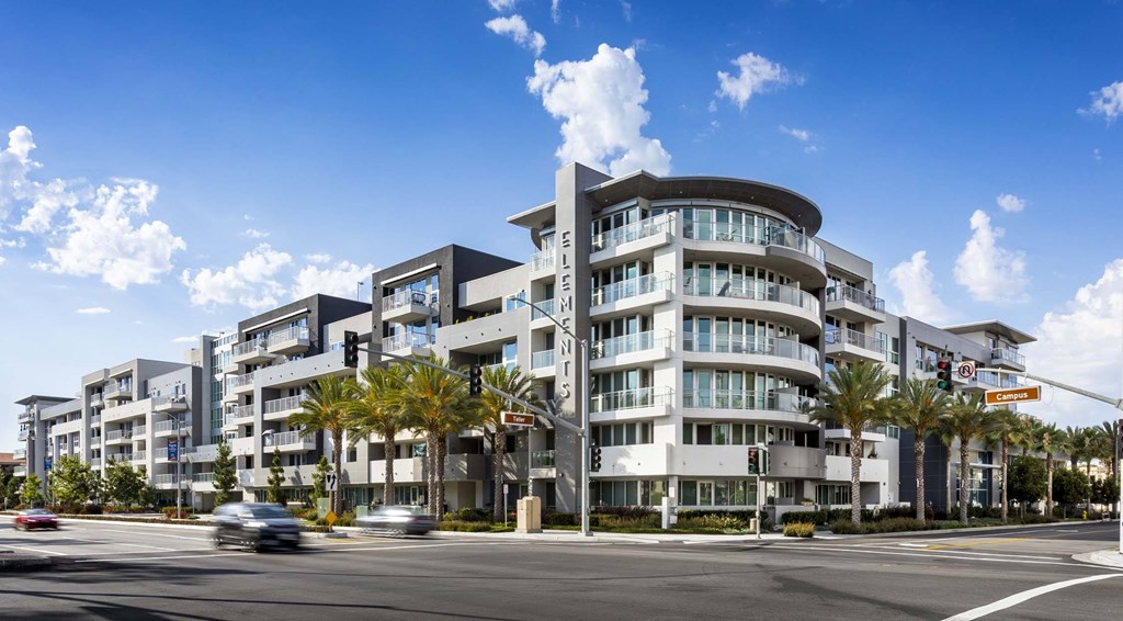 A modern apartment building with a curved design and palm trees in front.