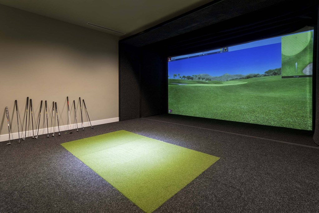 A room with a green carpet and a screen showing a golf course.