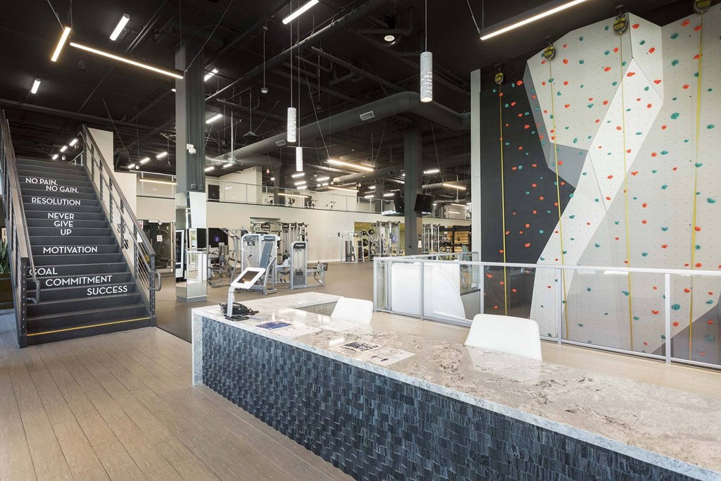 A climbing wall in a gym with a sign that says "No Pants Resolution" and "Never Give Up".