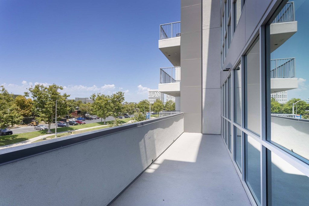 A balcony with a view of a parking lot and trees.