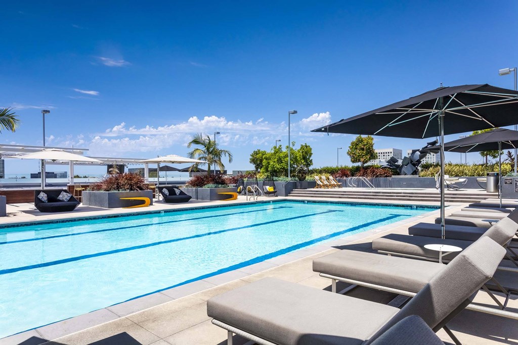 A pool with sun loungers and umbrellas is surrounded by a clear blue sky.