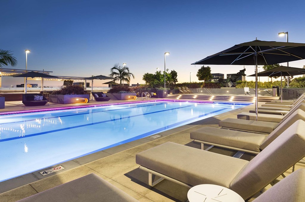 A pool with sun loungers and umbrellas is lit up with blue lights.