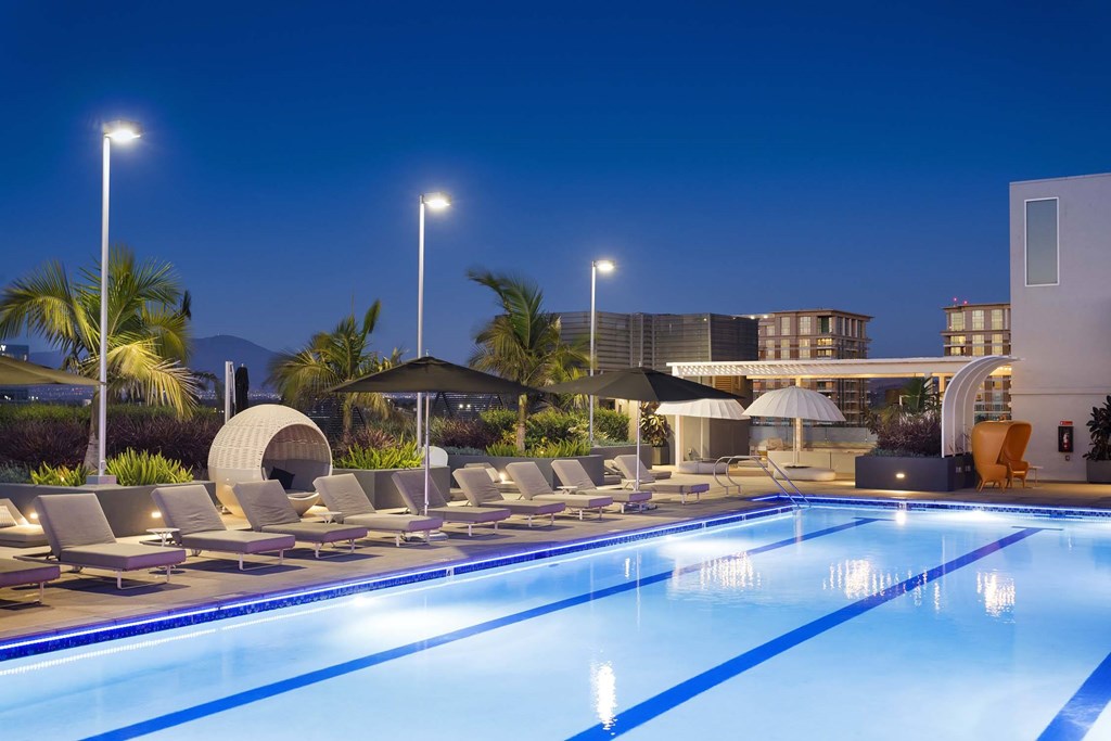 A swimming pool with lounge chairs and umbrellas in front of a building.