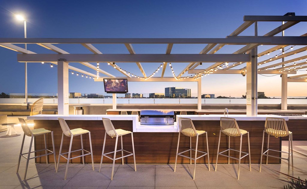 A bar with white chairs and a wooden counter is set up on a rooftop.