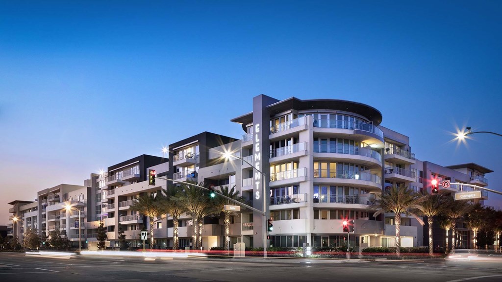 A modern multi-story building with balconies and palm trees in front.