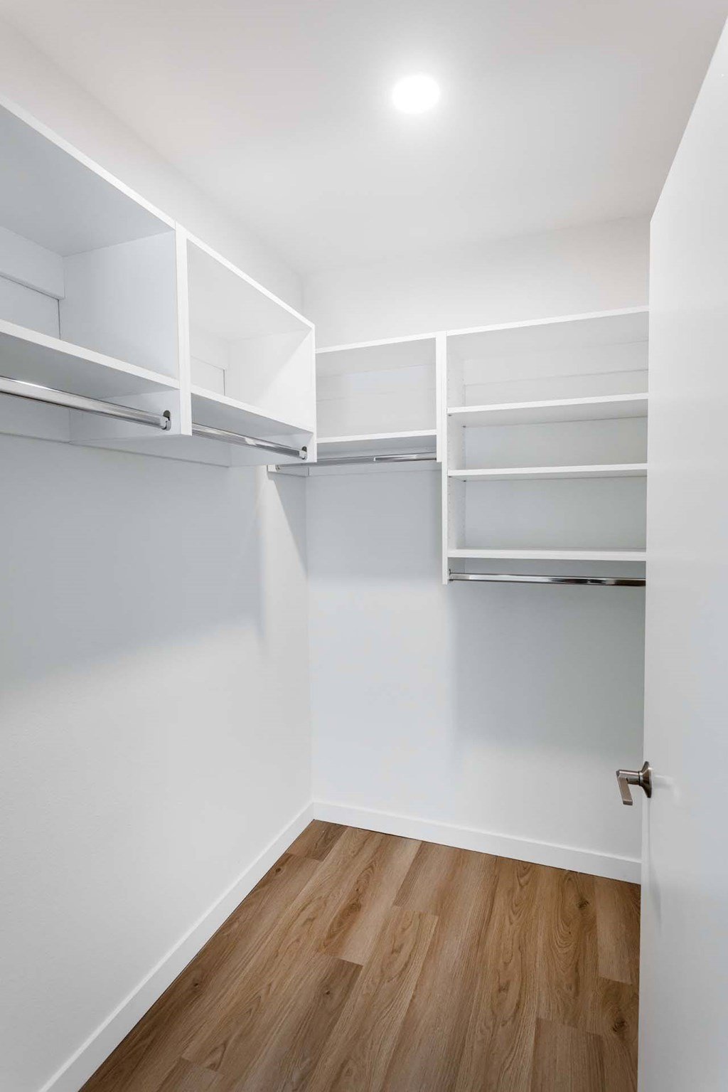 A white closet with shelves and a wooden floor.