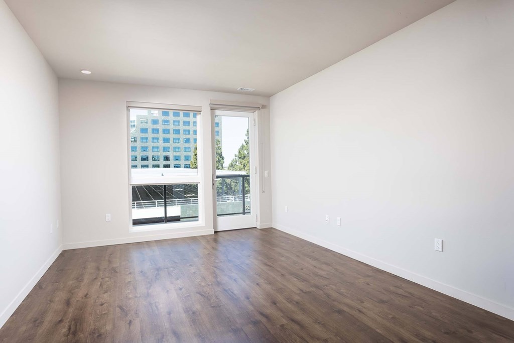 Empty room with a large window and wooden floor.