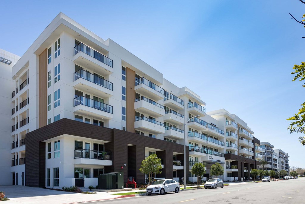 A row of modern apartment buildings with cars parked in front.