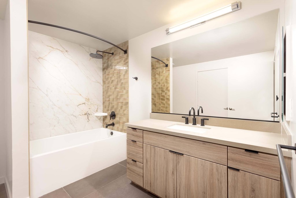 A bathroom with a marble wall and a white bathtub.