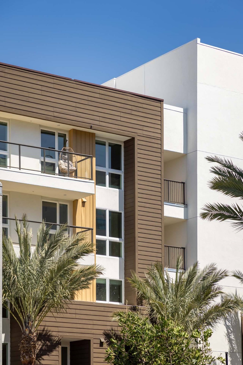 A modern building with a balcony and palm trees in front.