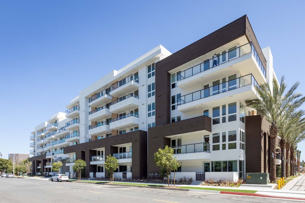 A modern multi-story apartment building with balconies and palm trees in front.