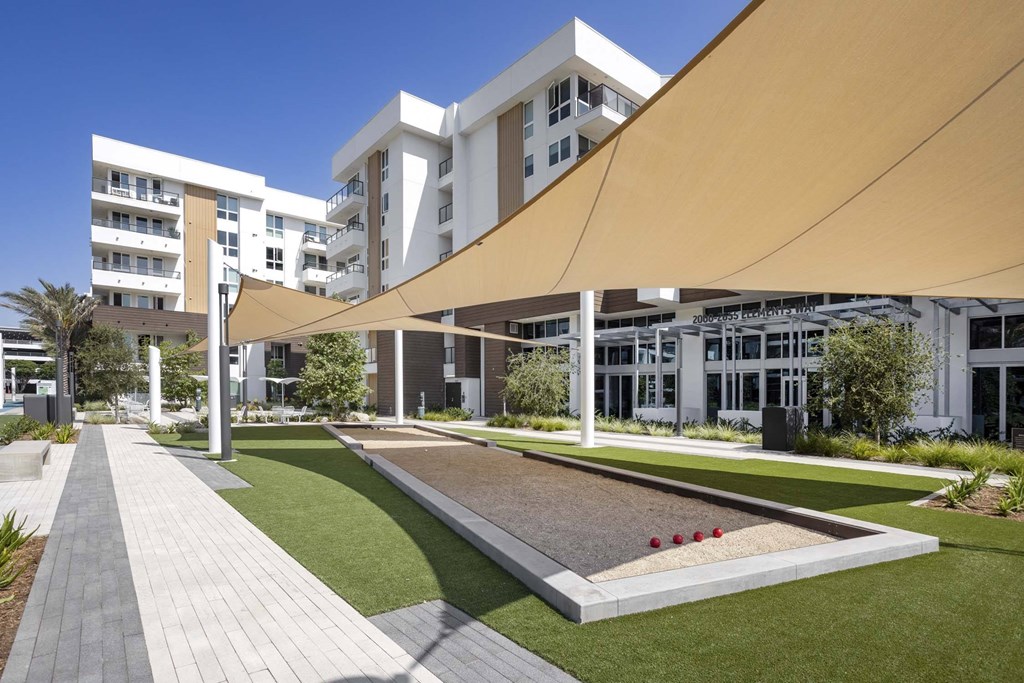 A modern building with a white facade and a long walkway with a grassy area and a water feature.