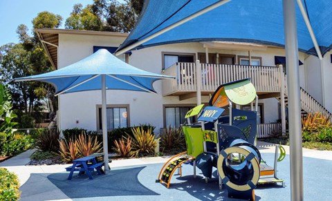 A playground with a blue umbrella and a slide.