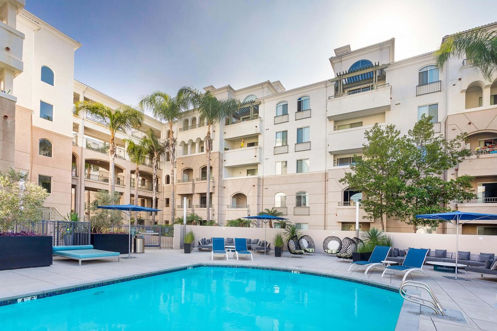A swimming pool in front of a building with a blue umbrella. at La Jolla Crossroads Apartments, San Diego, 92122