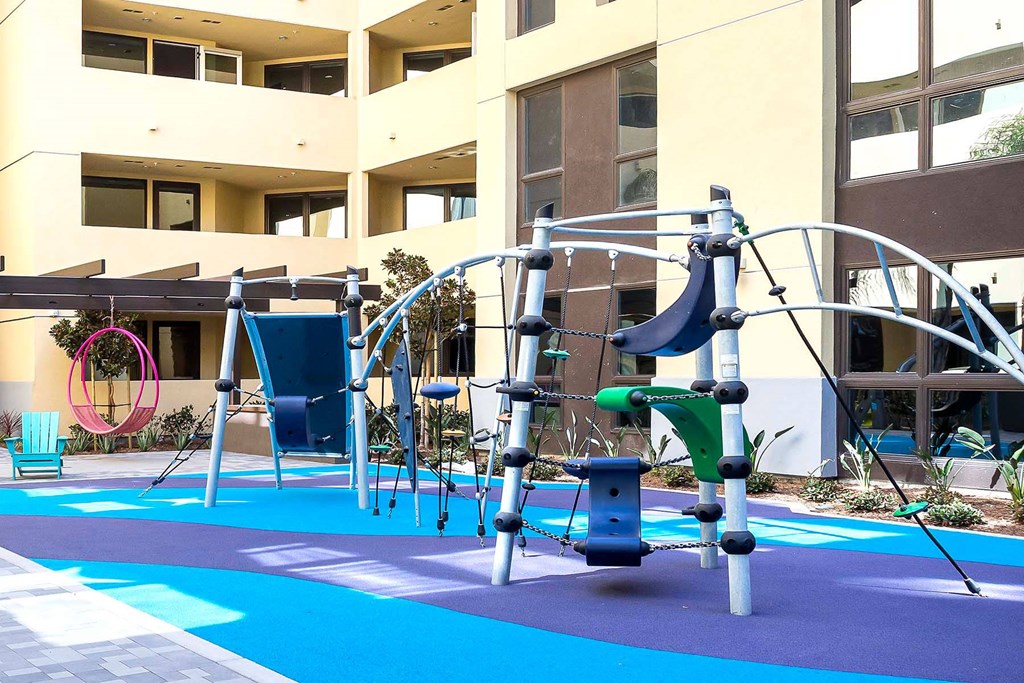 A playground with a slide and swings in front of a building.