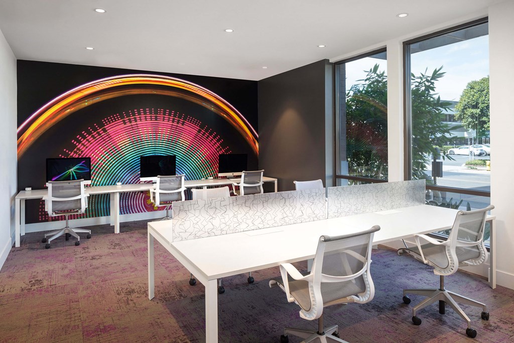 A conference room with a white table and chairs and a colorful light installation on the wall.