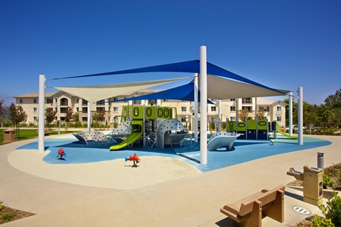 Shaded playground with colorful equipment and slides at Torrey Gardens Apartments, San Diego, CA 92130