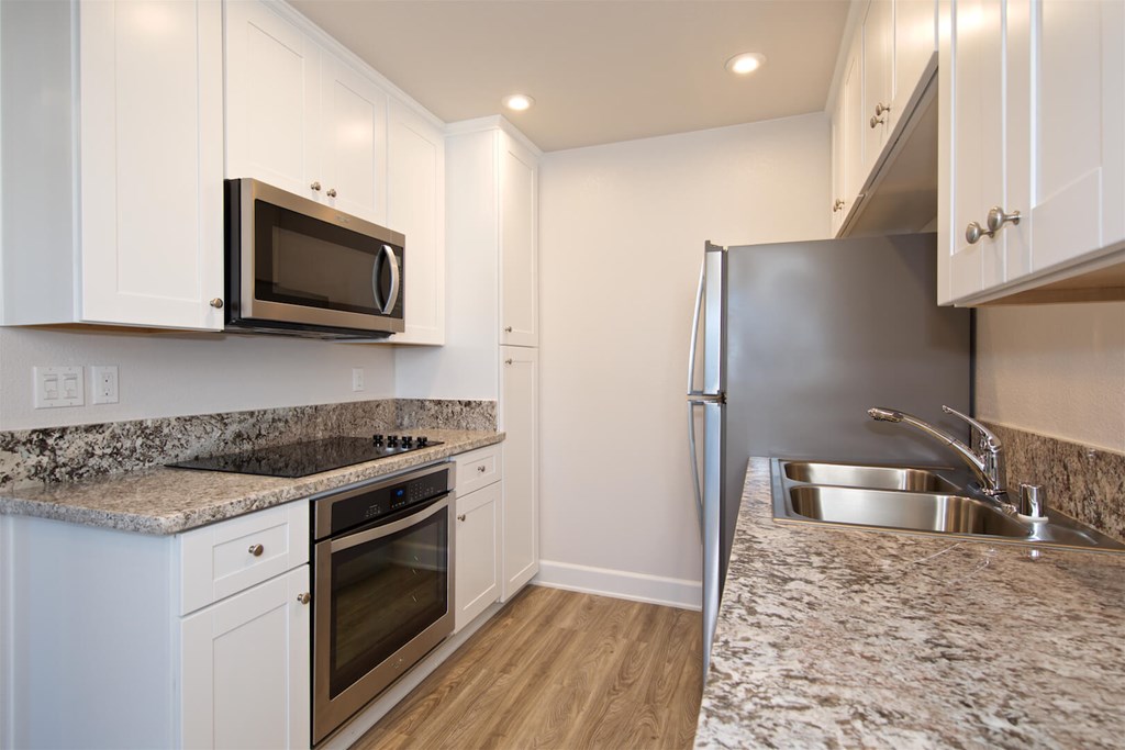 A kitchen with a refrigerator, microwave, oven, and sink.