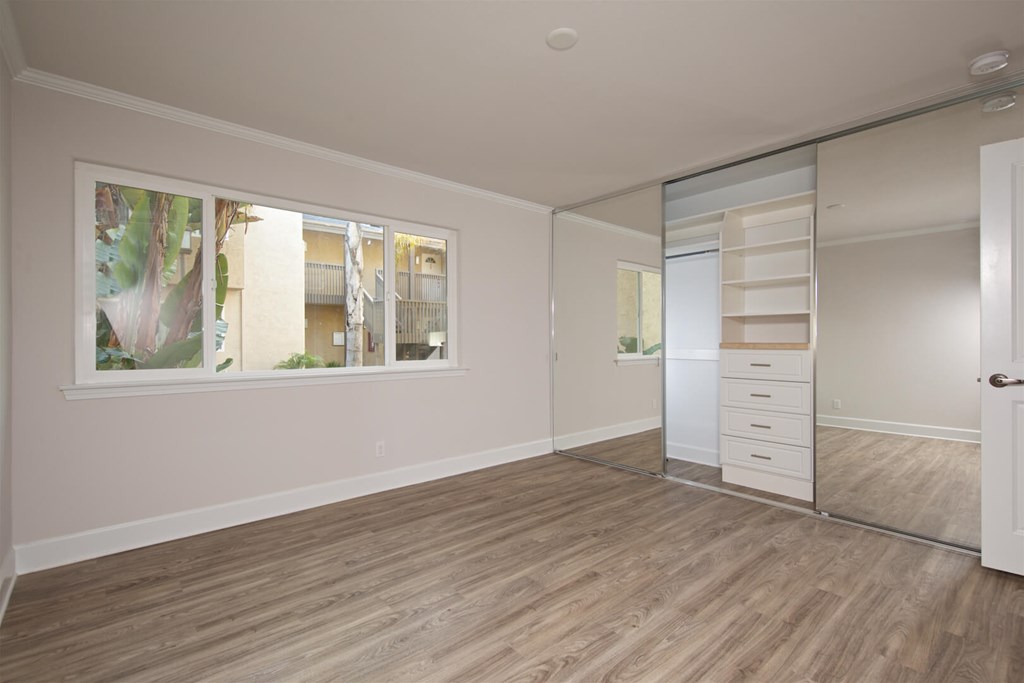 A room with wooden flooring and a large window with a view of a building outside.