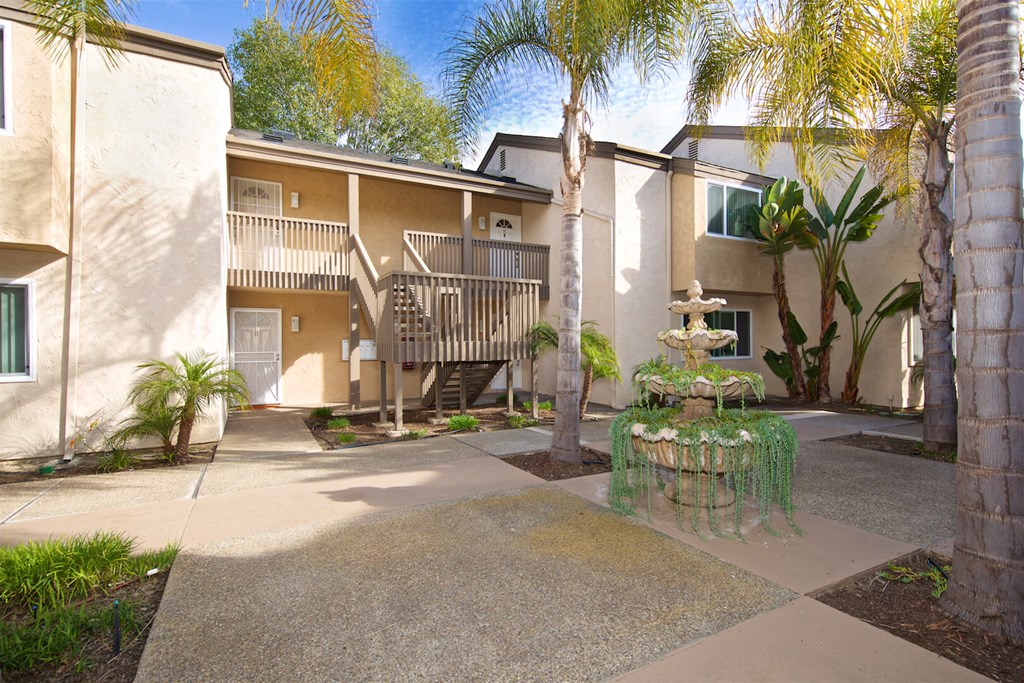 A courtyard with a fountain surrounded by palm trees and apartment buildings.