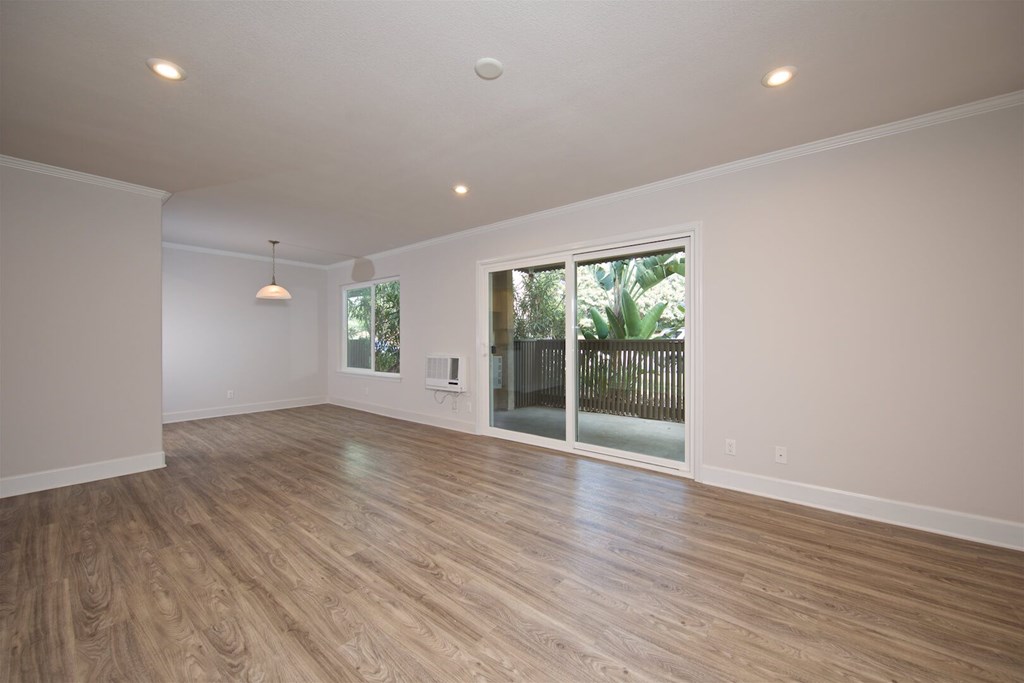 A room with wooden flooring and a sliding glass door leading to a backyard.