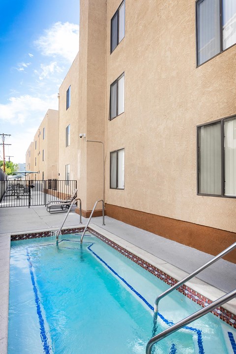A swimming pool in front of a tan building with a metal railing.